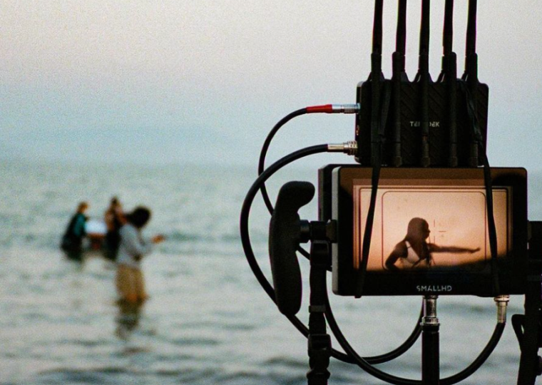 Camera equipment is pointed toward 3 people who are standing in a body of water