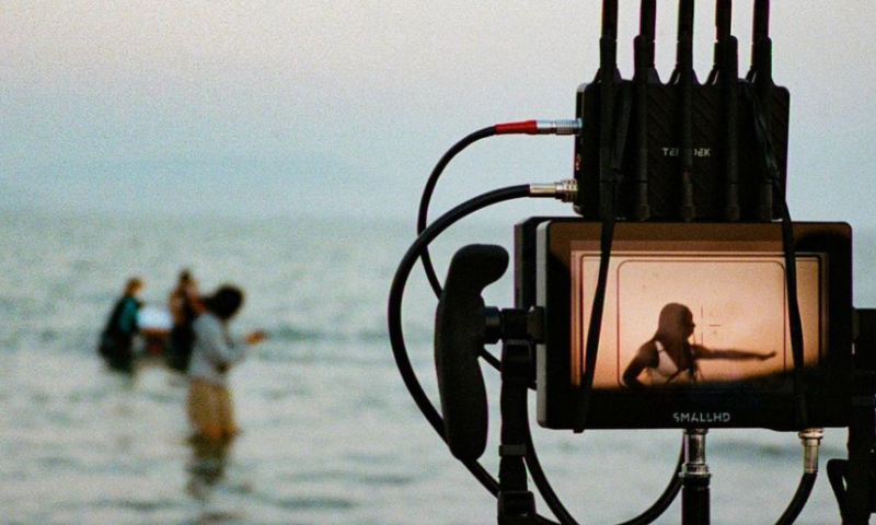 Camera equipment is pointed toward 3 people who are standing in a body of water
